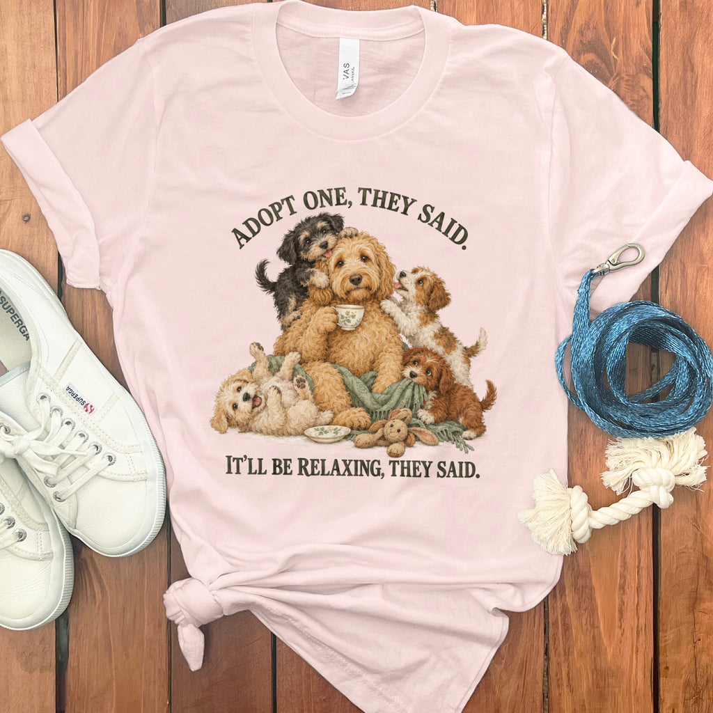 Pink t-shirt with illustration of dogs and text: "ADOPT ONE, THEY SAID. IT'LL BE RELAXING, THEY SAID."