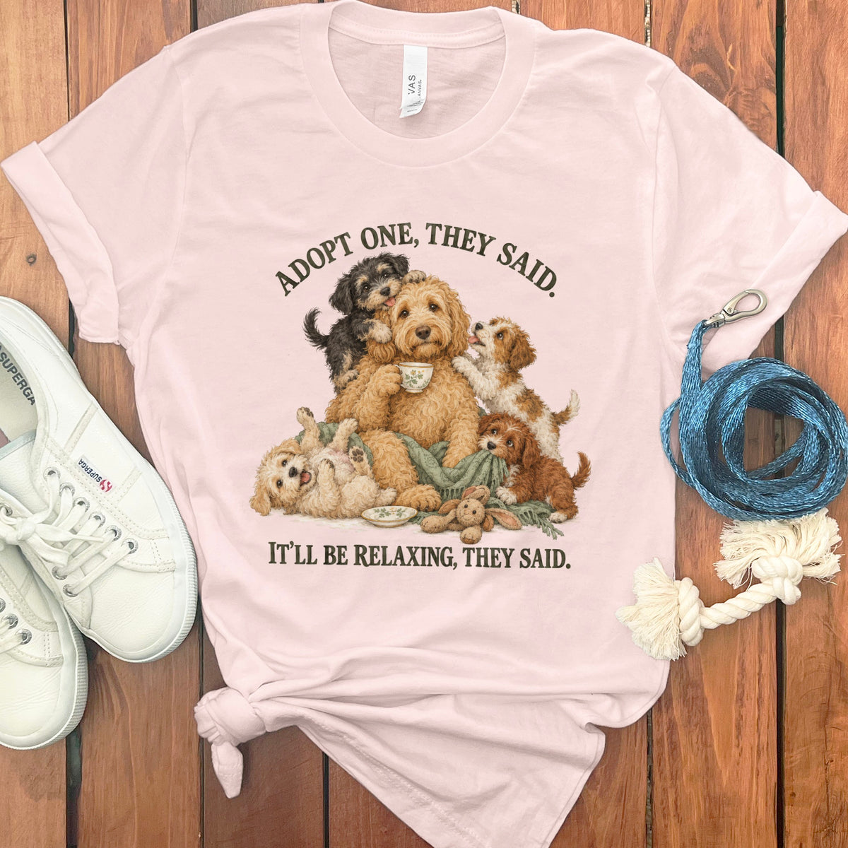 Pink t-shirt with illustration of dogs and text: "ADOPT ONE, THEY SAID. IT'LL BE RELAXING, THEY SAID."
