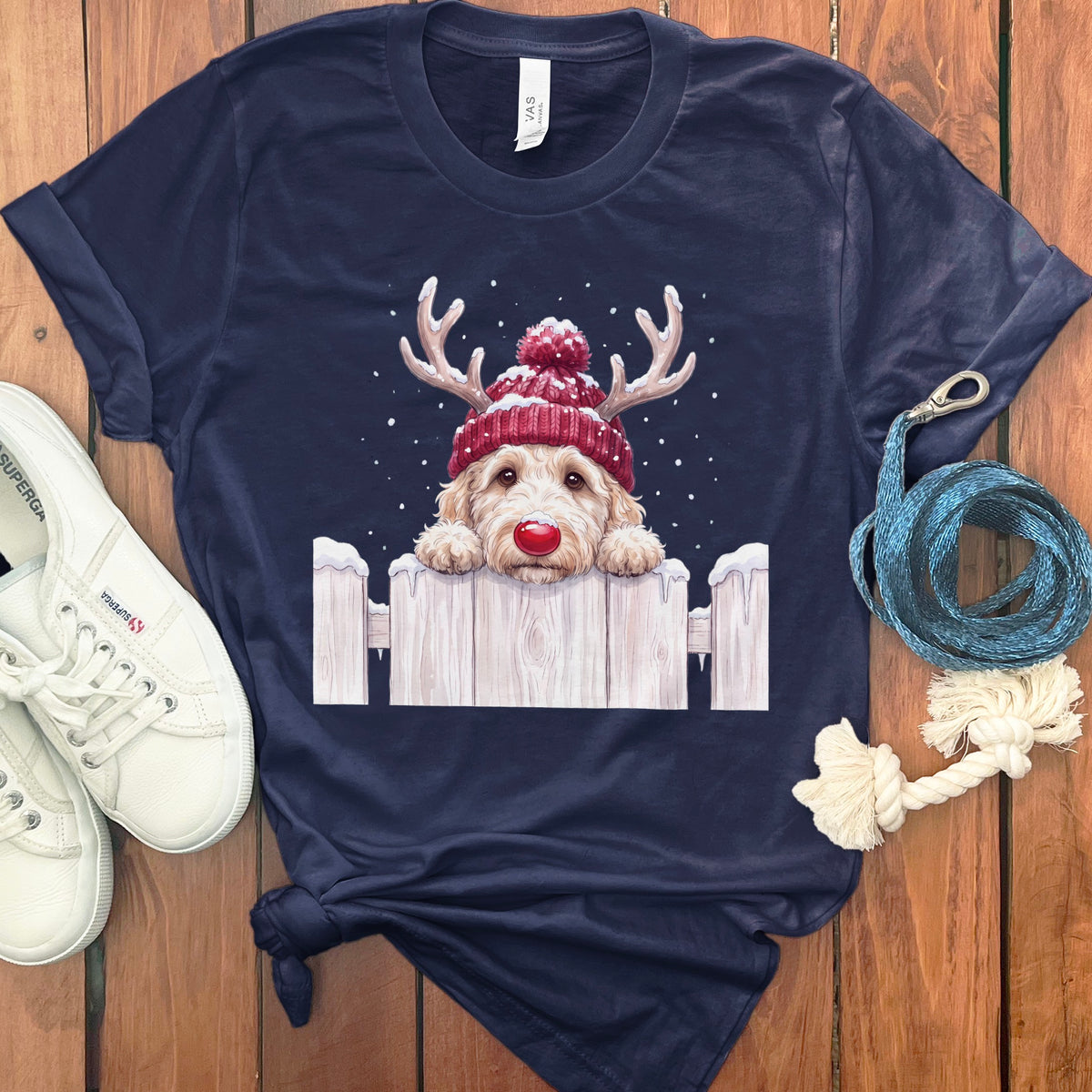 Navy t-shirt with a doodle dog wearing a Christmas hat and antlers, peeking over a fence.
