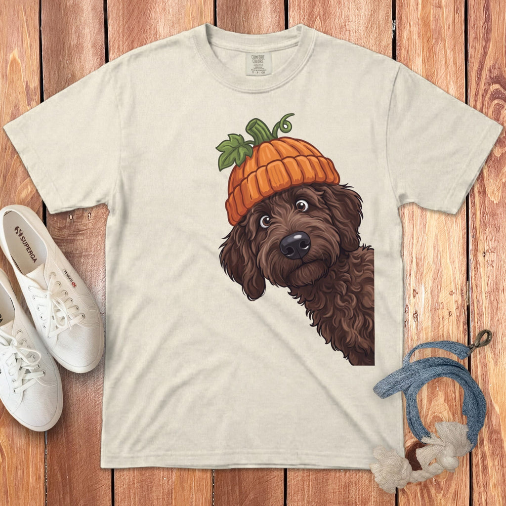 Light tan t-shirt with brown dog wearing a pumpkin hat, next to white sneakers.