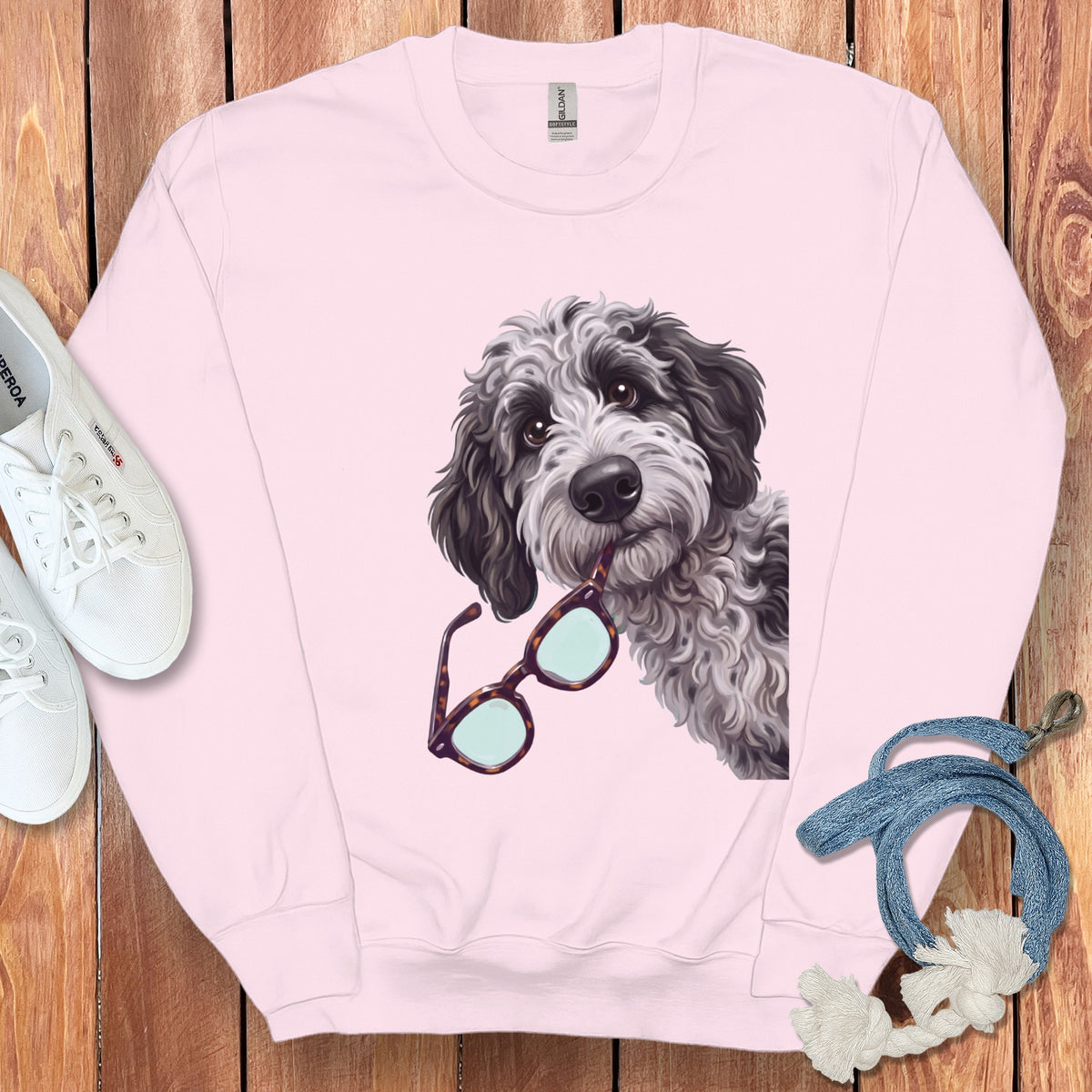 Light pink crewneck sweatshirt featuring a graphic of a black and white doodle dog holding glasses in its mouth.