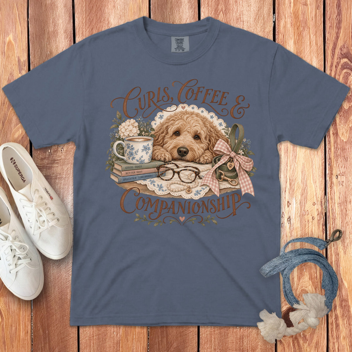 A slate blue t-shirt featuring a goldendoodle graphic, white sneakers, and a leash on a wooden background.