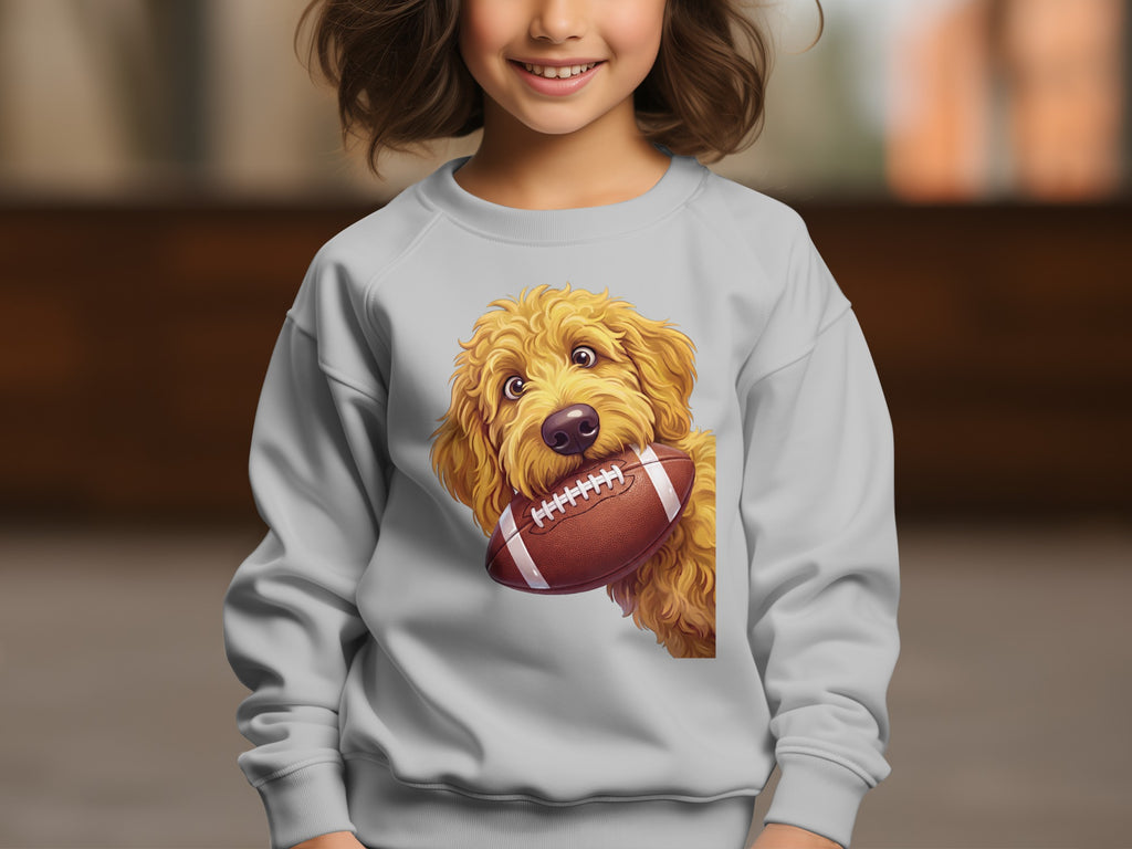 Golden doodle holding a football on a gray sweatshirt.