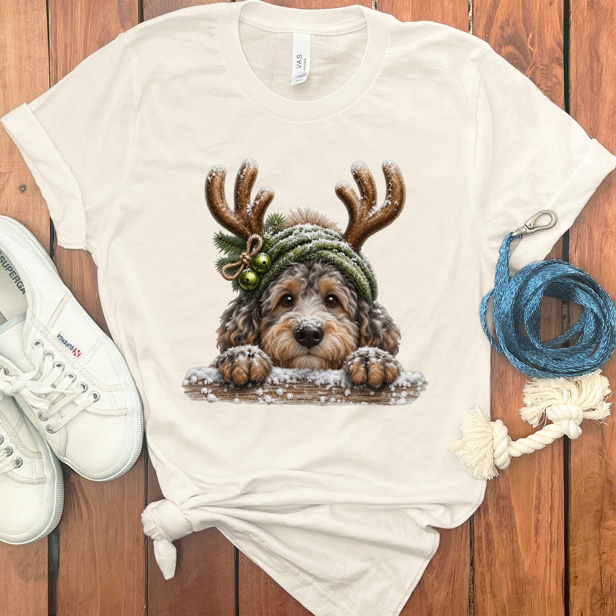 Fluffy dog wearing reindeer antlers and a knit hat on a cream shirt.