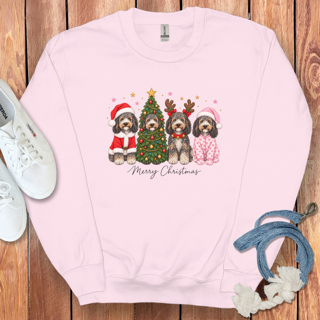Light pink crewneck sweatshirt featuring a graphic of four doodle dogs celebrating Christmas, surrounded by white sneakers and a dog leash on a wooden background.