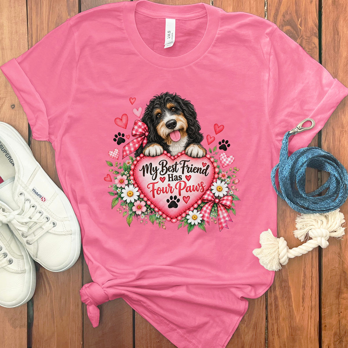 A pink t-shirt featuring a bernedoodle graphic, heart text reading My Best Friend Has Four Paws, white sneakers, and a blue leash.
