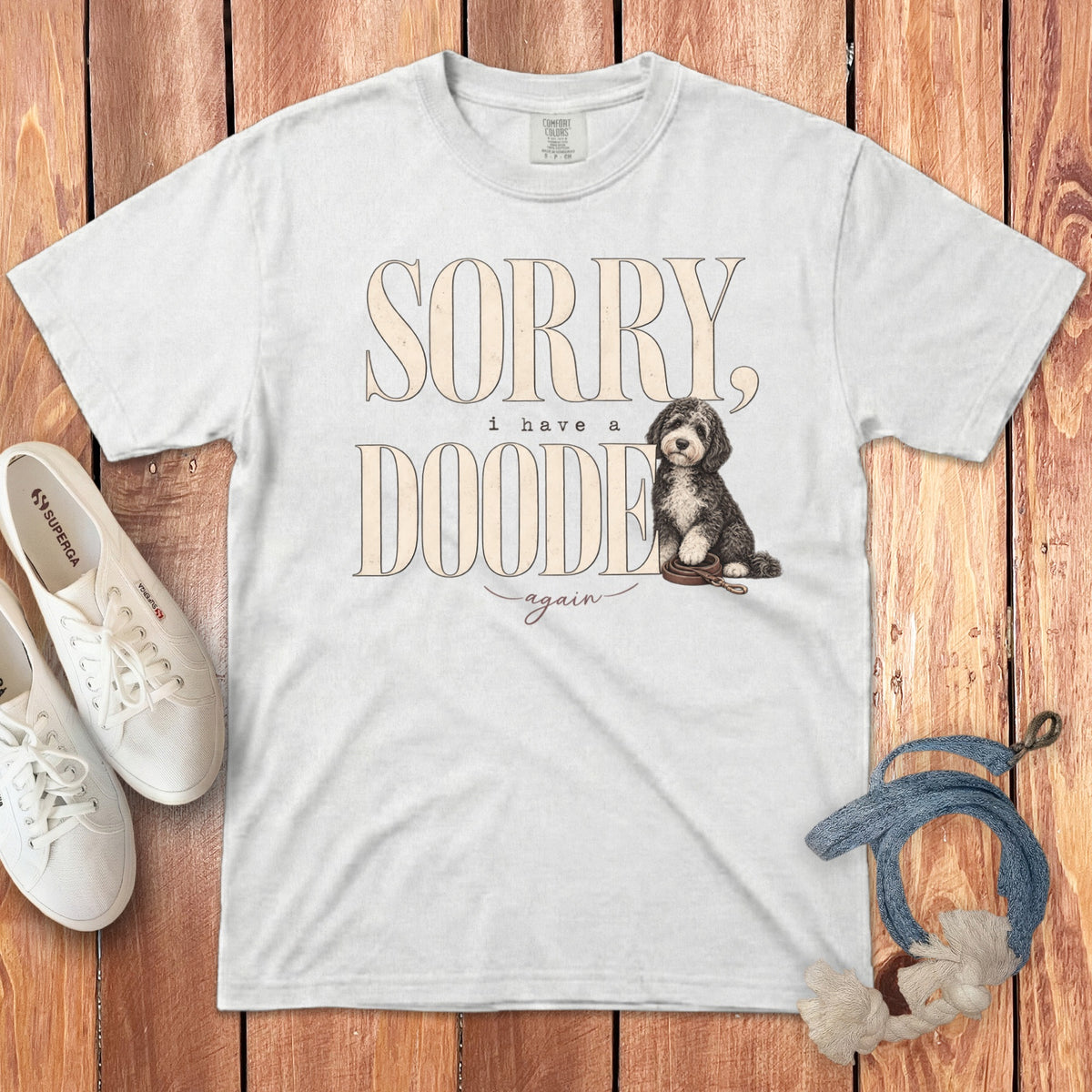 White crewneck t-shirt with Sorry, I have a doodie again text and doodle dog graphic on wooden background.
