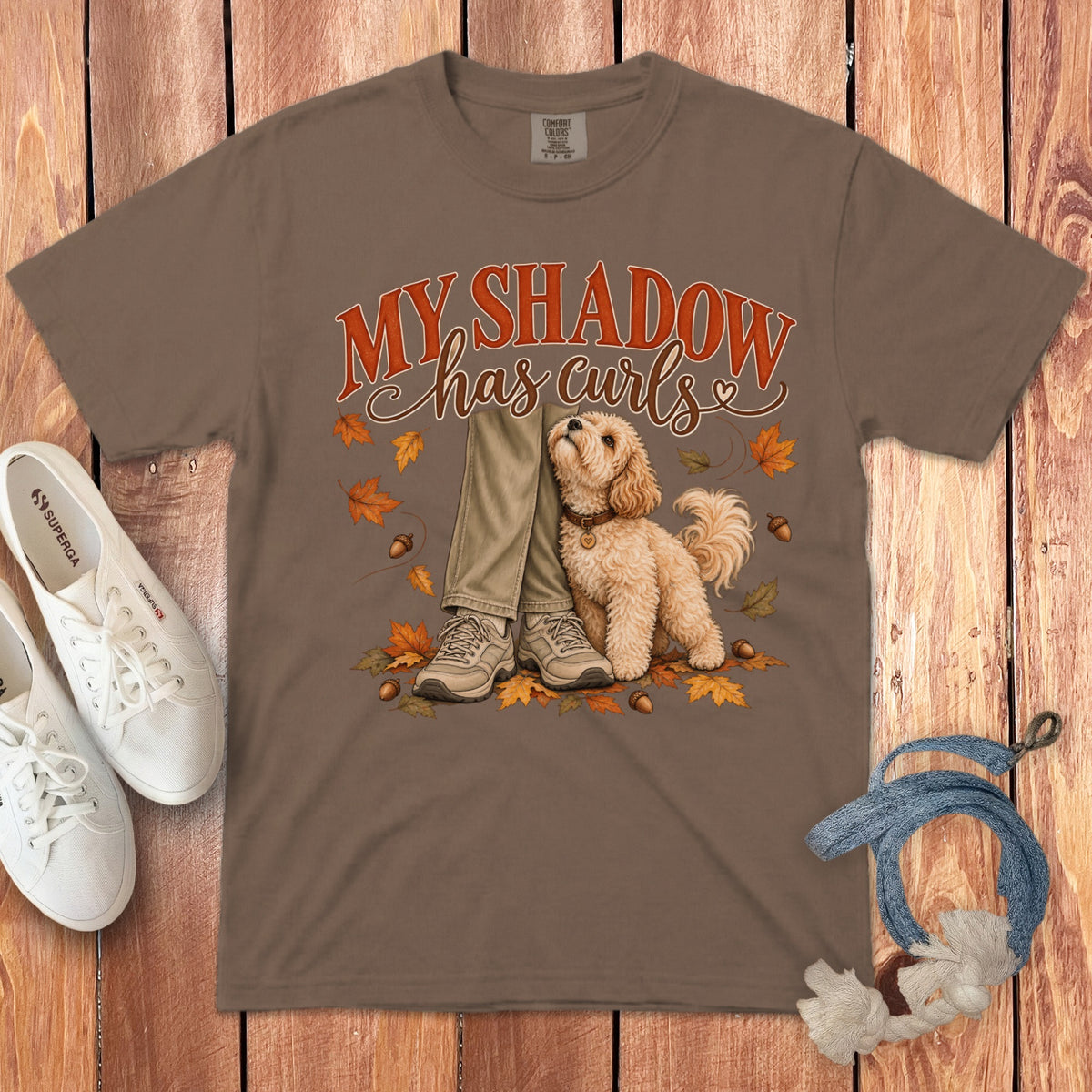 Brown t-shirt featuring a graphic of a curly doodle dog next to legs, with autumn leaves and text that reads My Shadow has curls.