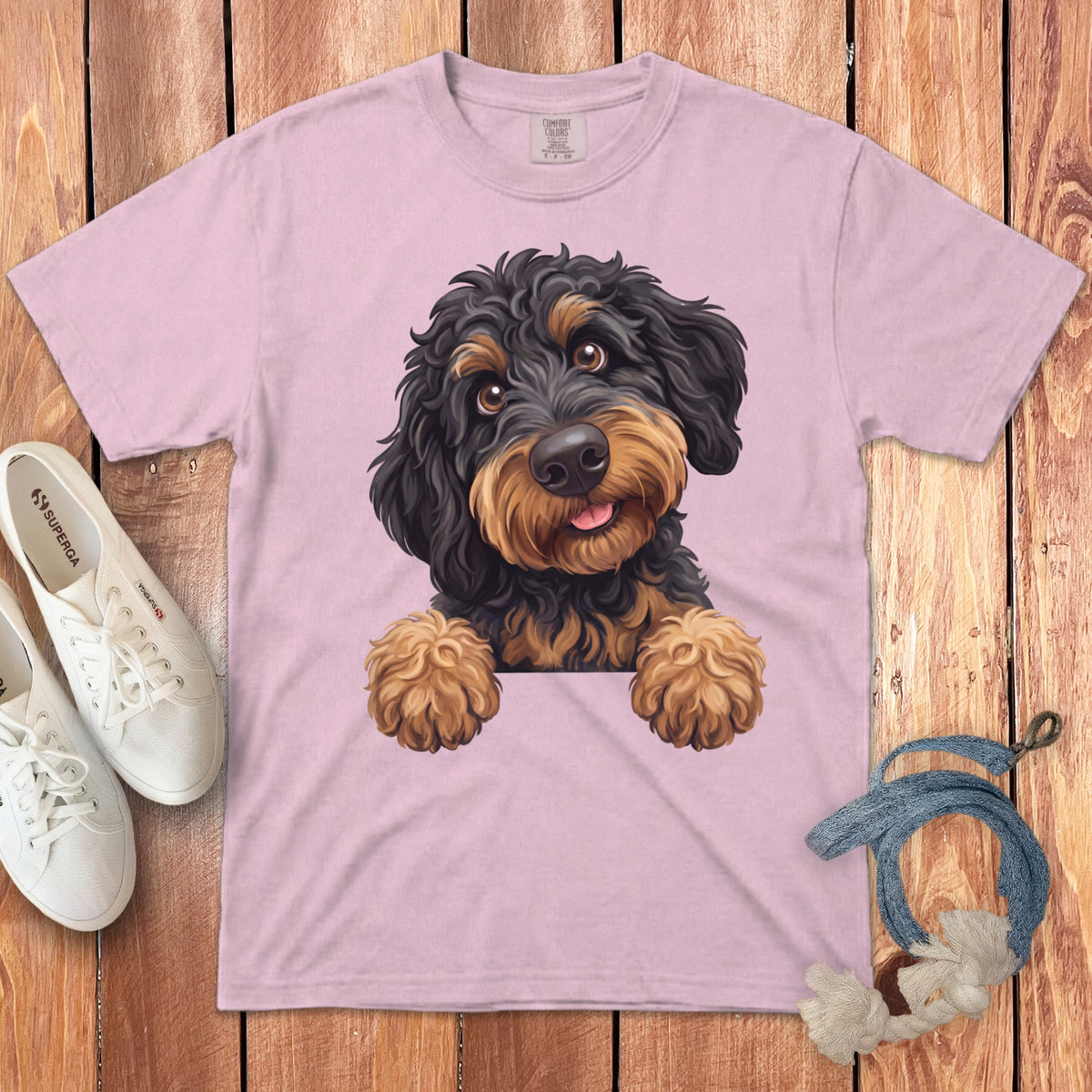 Pink t-shirt with a printed illustration of a fluffy black and tan dog peeking over the edge.