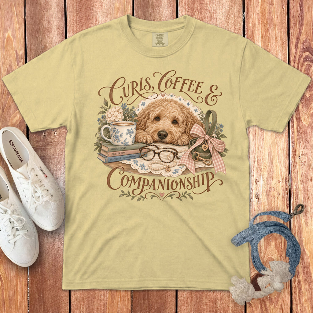 A pale yellow t-shirt featuring a vintage illustration of a fluffy golden doodle dog, books, and coffee.