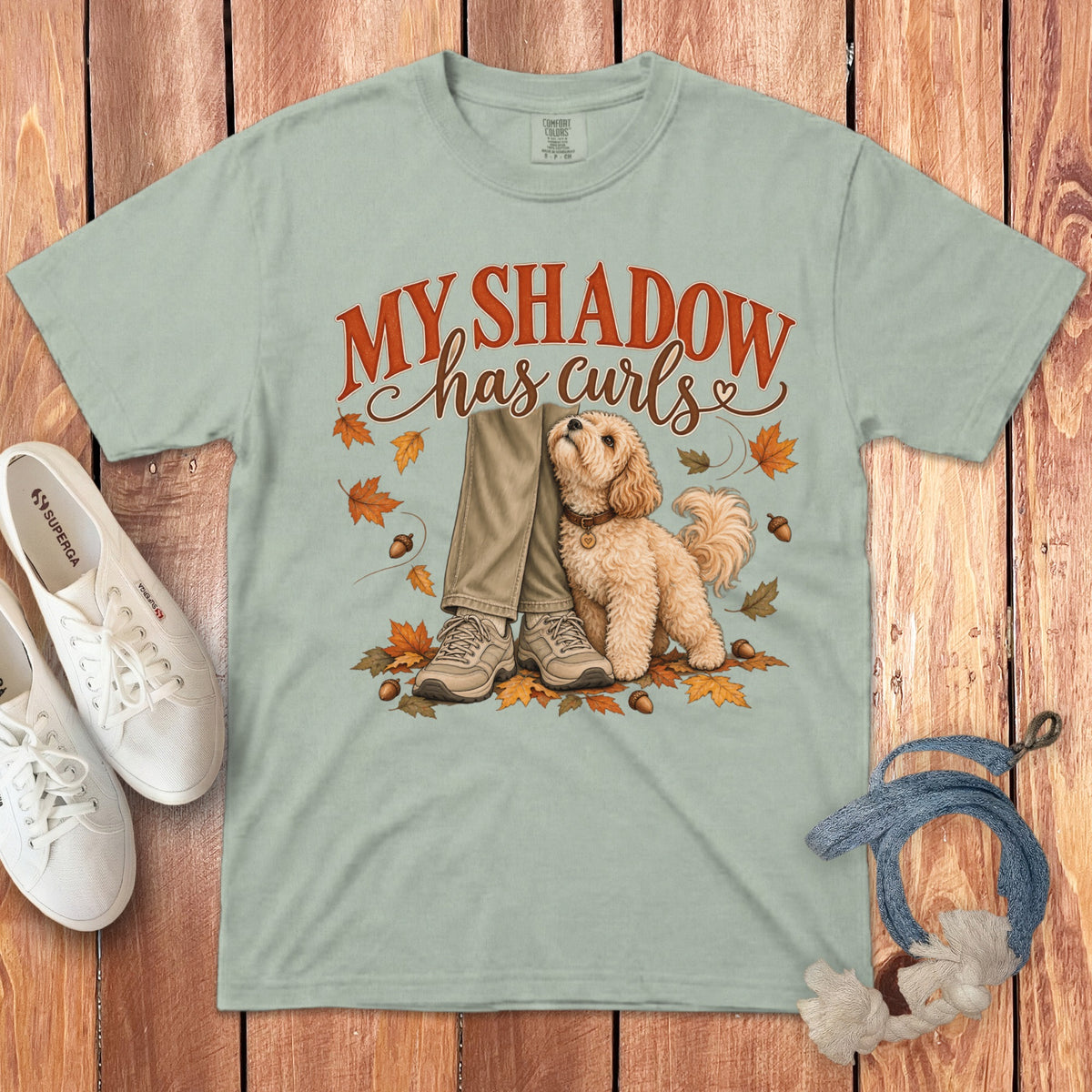 Light green t-shirt with graphic of curly poodle, fall leaves, and text reading My shadow has curls.