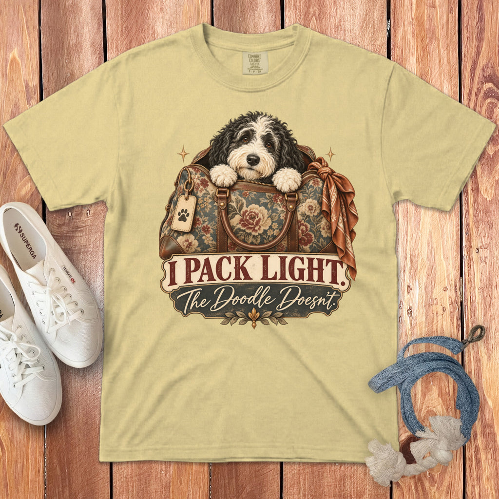 Light yellow t-shirt featuring a doodle dog inside a floral travel bag with text reading I Pack Light The Doodle Doesnt.