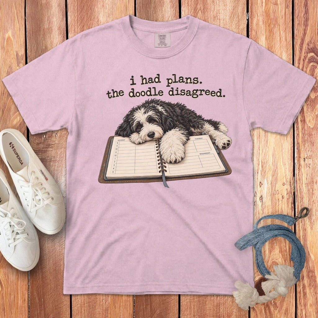 A pink t-shirt featuring a black and white doodle dog resting on an open planner.