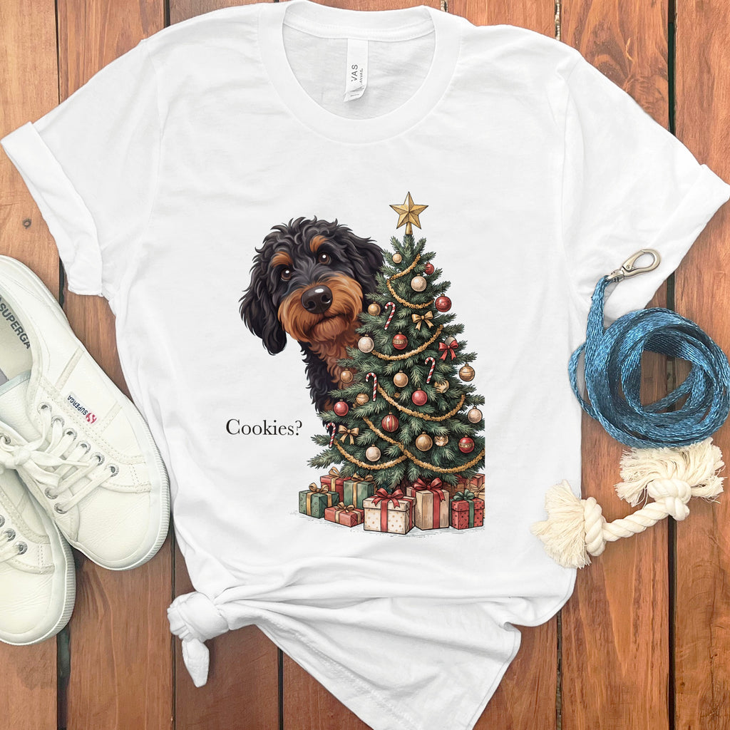 Dachshund peeking behind Christmas tree with gifts, text reads "Cookies?"