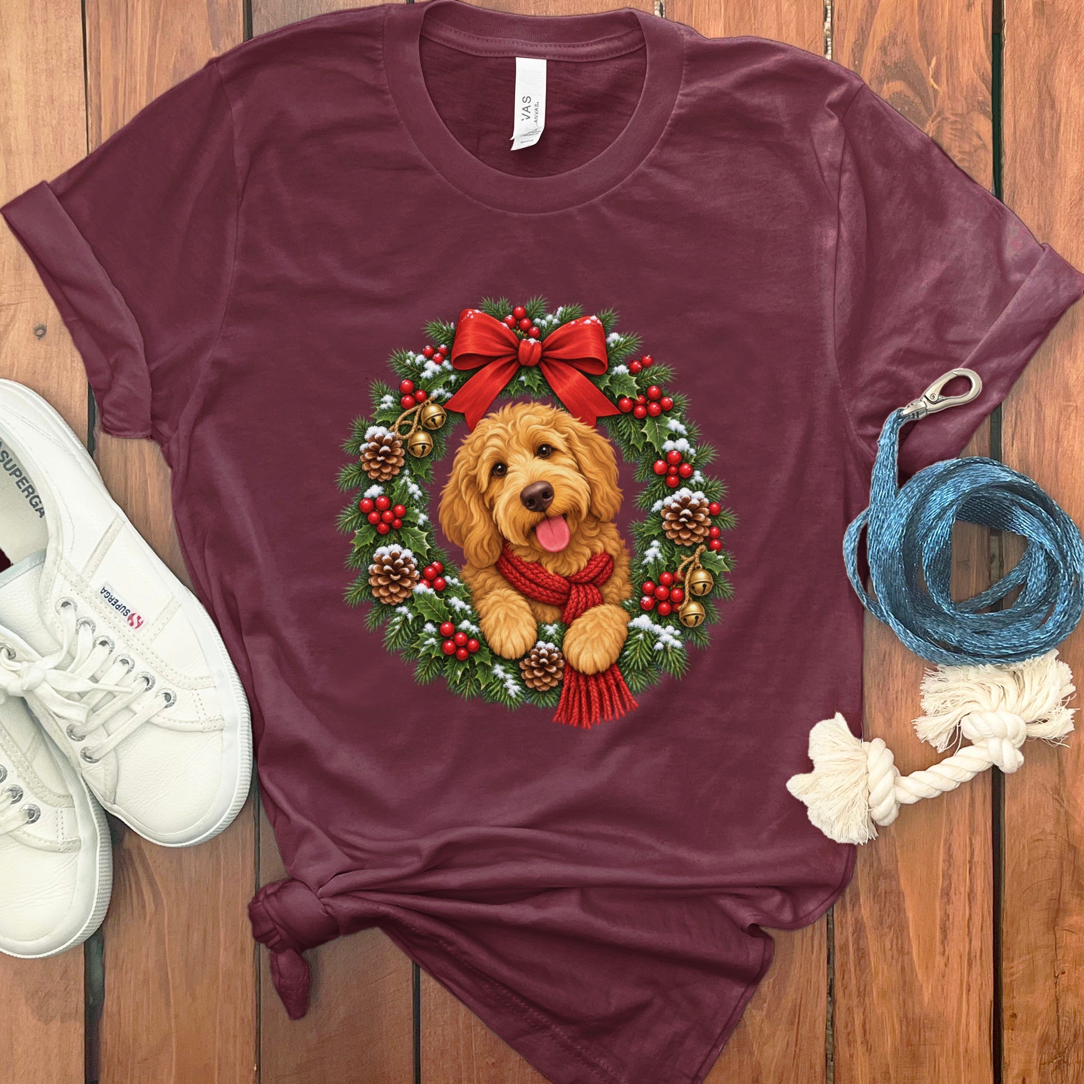 Maroon crewneck t-shirt featuring a Golden Doodle inside a Christmas wreath graphic on a wooden background.