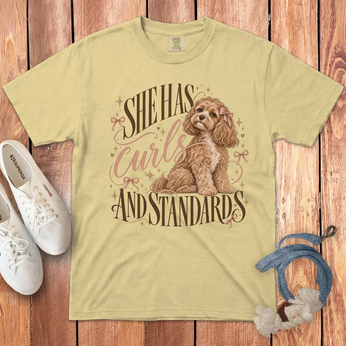 A yellow t-shirt features a graphic of a curly brown dog and the text She Has Curls And Standards.