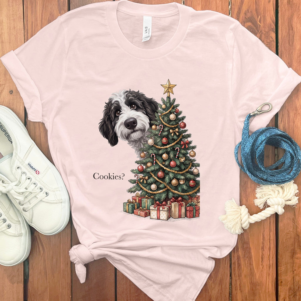 Black and white dog peeks from behind a decorated Christmas tree with presents and text "Cookies?".