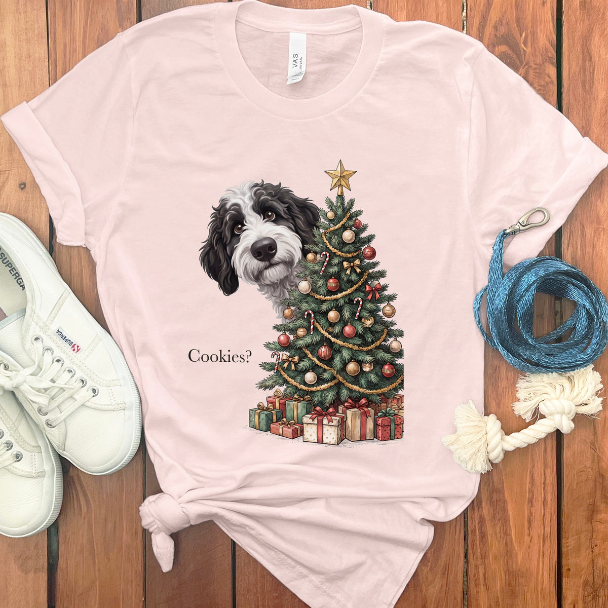 Black and white dog peeks from behind a decorated Christmas tree with presents and text "Cookies?".