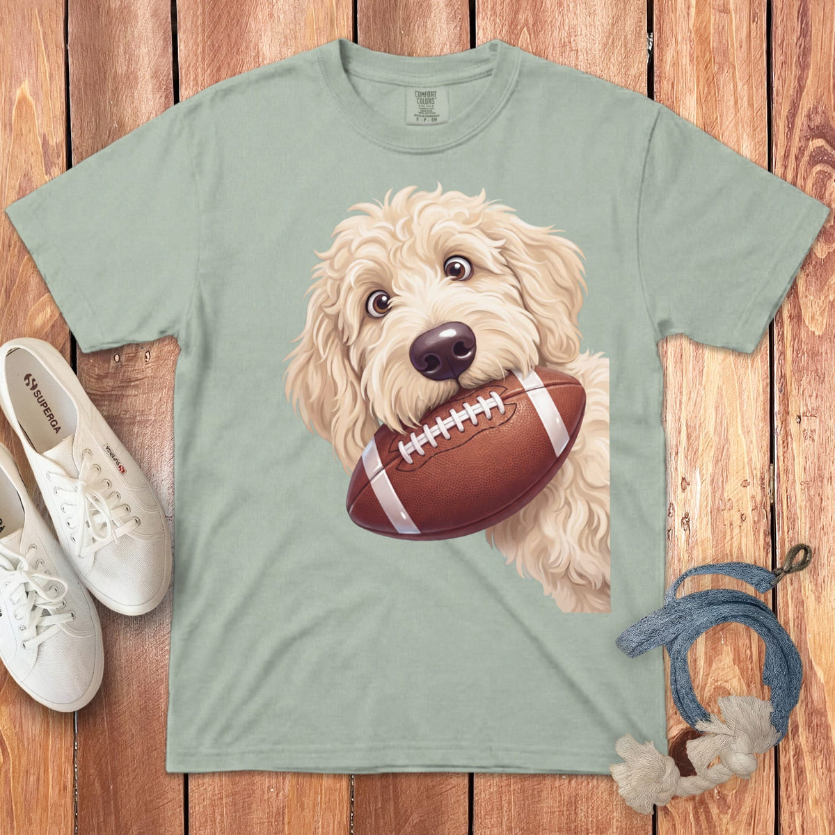 Light green t-shirt with a fluffy dog holding a football in its mouth.