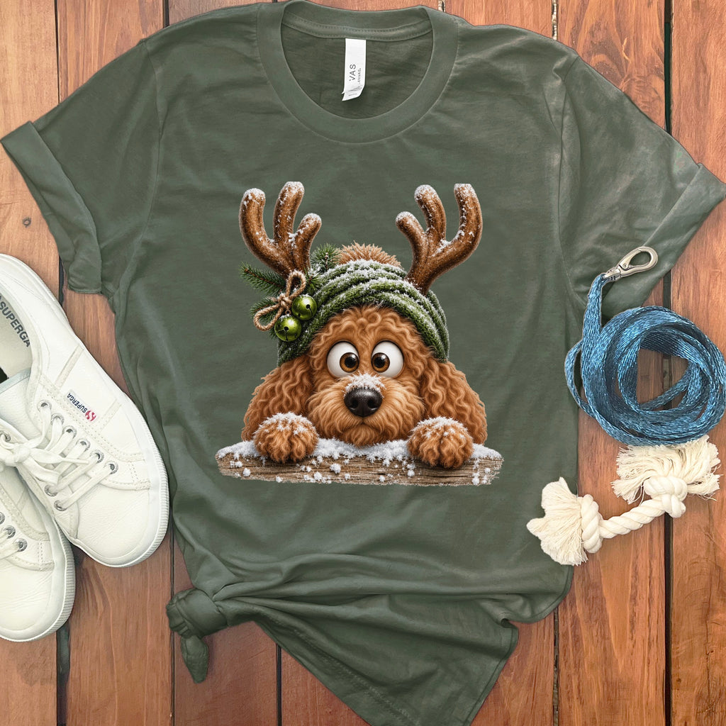 Brown poodle wearing reindeer antlers and a green beanie, peeking over a snowy log.