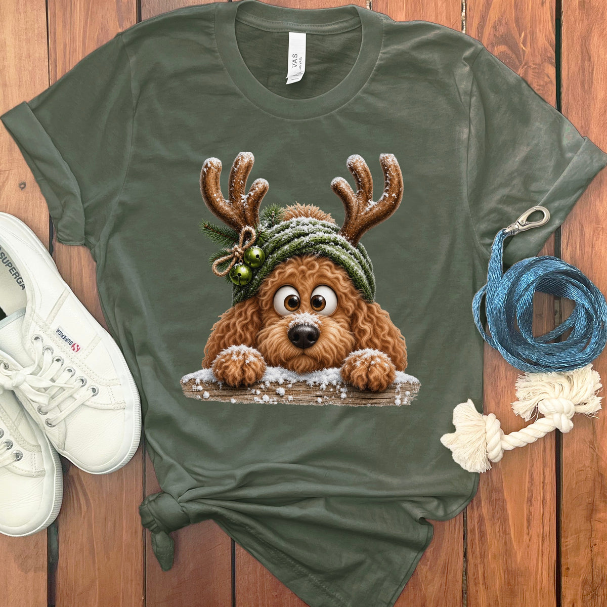Brown poodle wearing reindeer antlers and a green beanie, peeking over a snowy log.