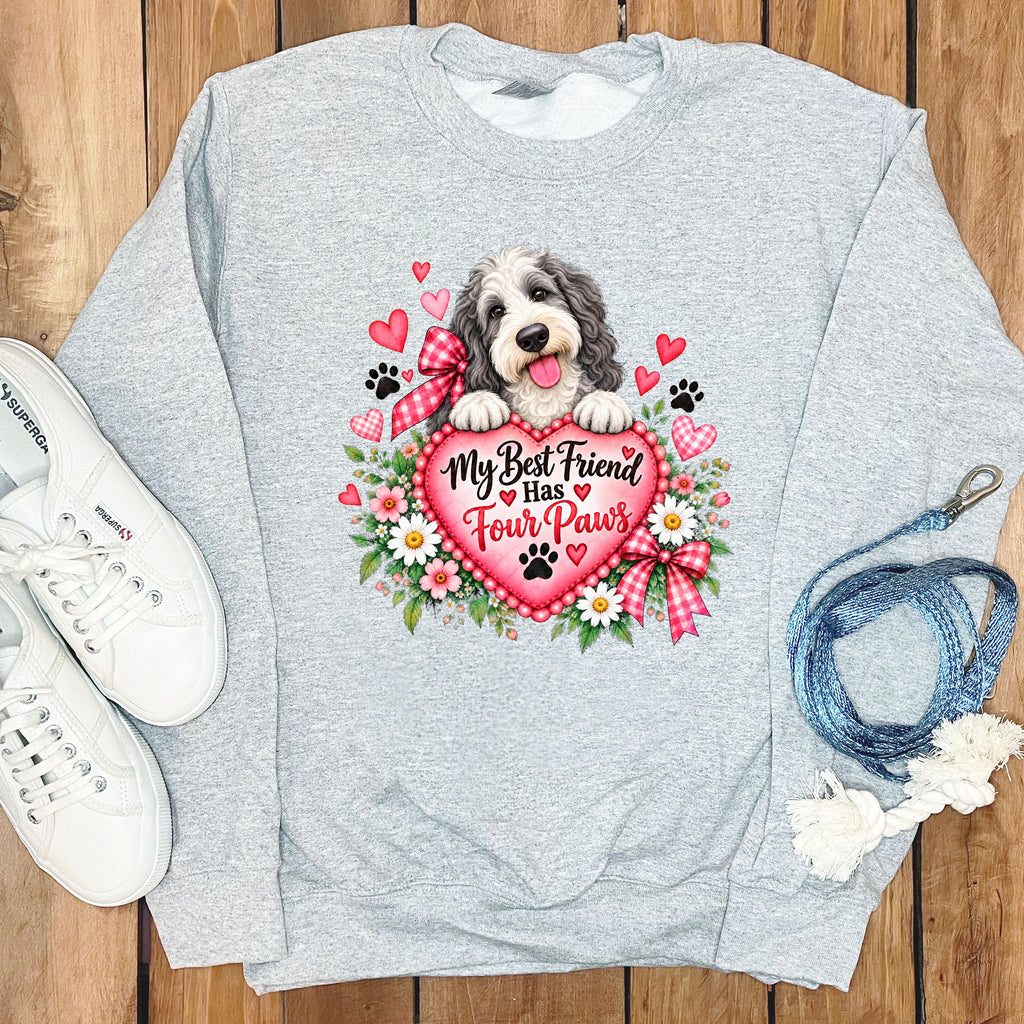 Heather gray crewneck sweatshirt featuring a graphic of a fluffy dog holding a pink heart with the text My Best Friend Has Four Paws surrounded by flowers and red hearts.