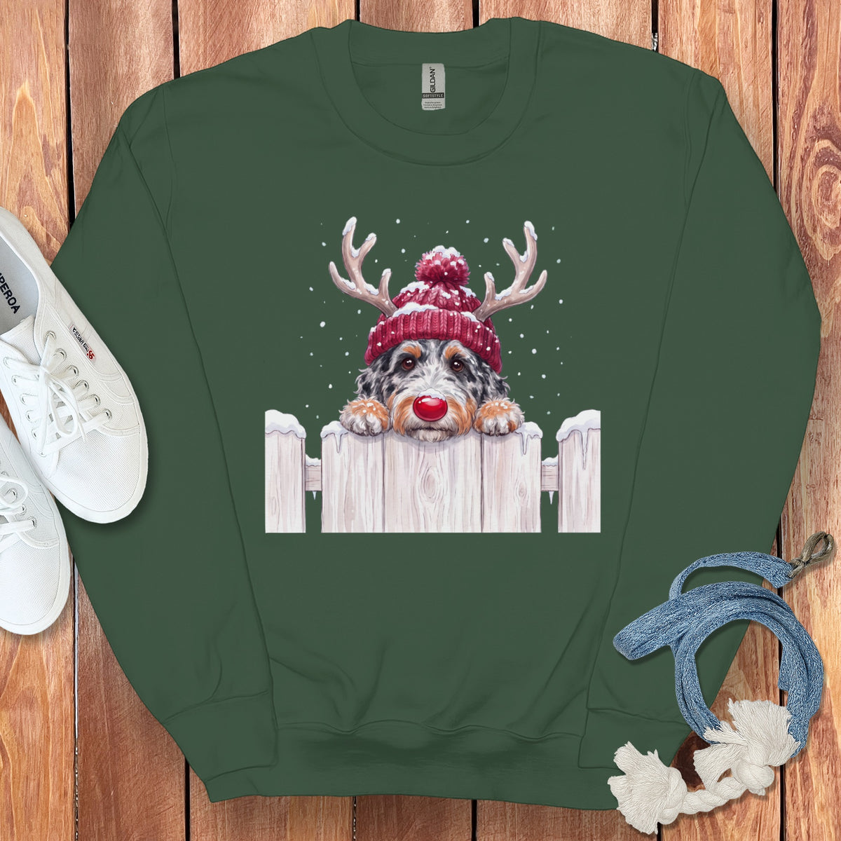 Green sweatshirt with dog wearing Santa hat and antlers on a white picket fence.