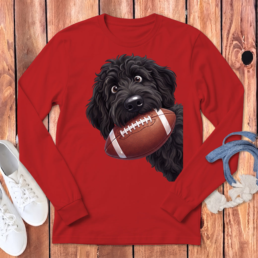 Black poodle with football in mouth on red long-sleeve shirt.