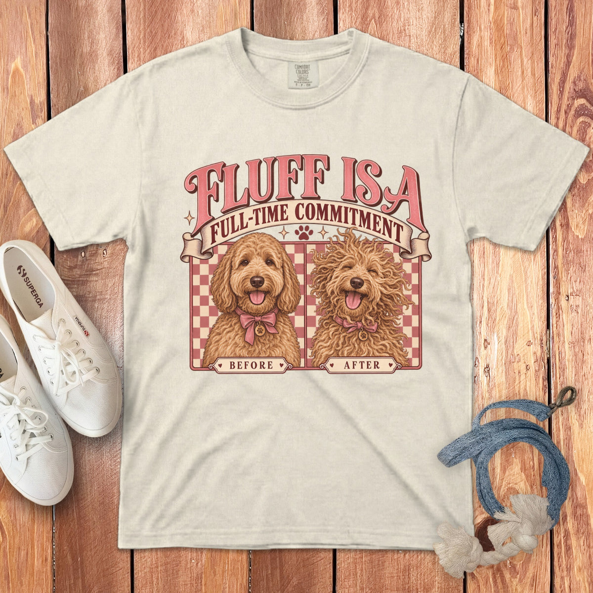 An off-white t-shirt with a graphic of two labradoodles labeled "Before" and "After," featuring the text "Fluff is a full-time commitment."