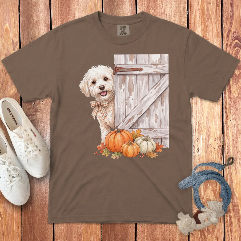 Brown t-shirt with a watercolor graphic of a fluffy dog peeking from behind a rustic door with pumpkins and autumn leaves.