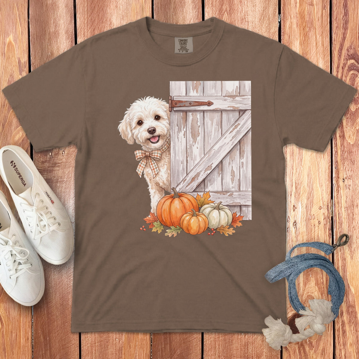 Brown t-shirt with a watercolor graphic of a fluffy dog peeking from behind a rustic door with pumpkins and autumn leaves.