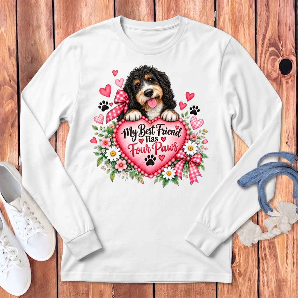 A white long-sleeve t-shirt with a graphic of a Bernedoodle holding a pink heart that reads, My Best Friend Has Four Paws.