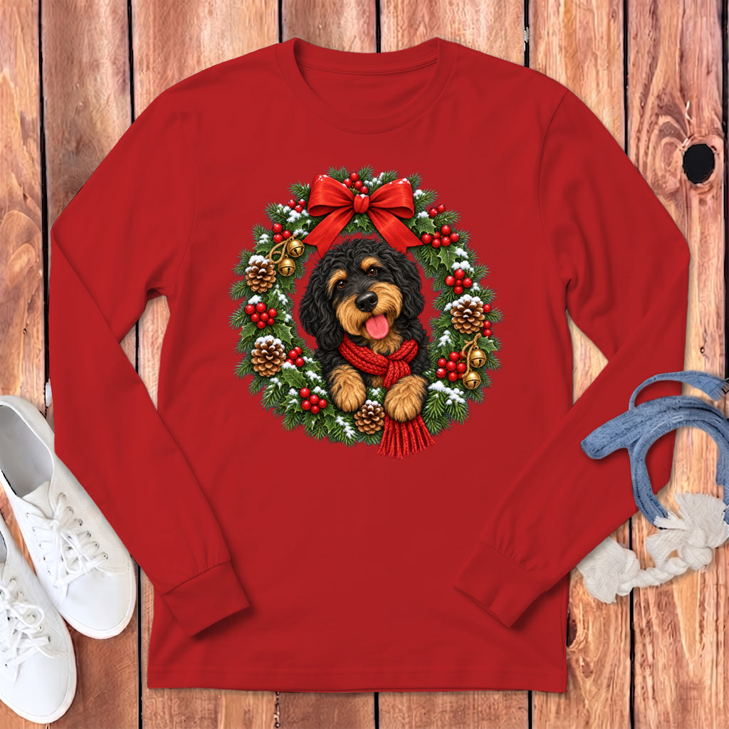 Red long-sleeved shirt featuring a fluffy black and tan dog wearing a red scarf inside a Christmas wreath.