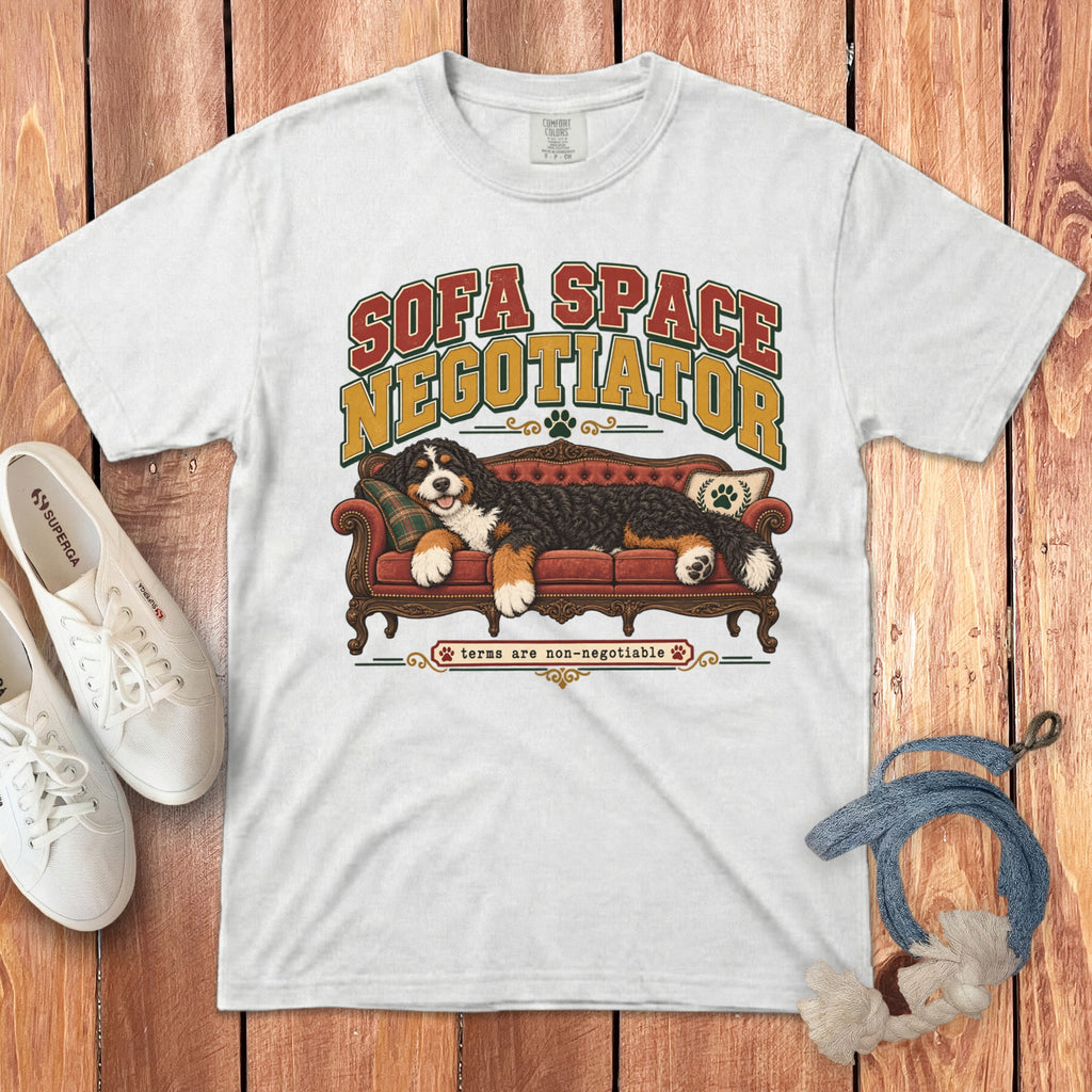 A white crewneck t-shirt featuring graphic text that reads Sofa Space Negotiator and a Bernese Mountain Dog lying on a red couch.
