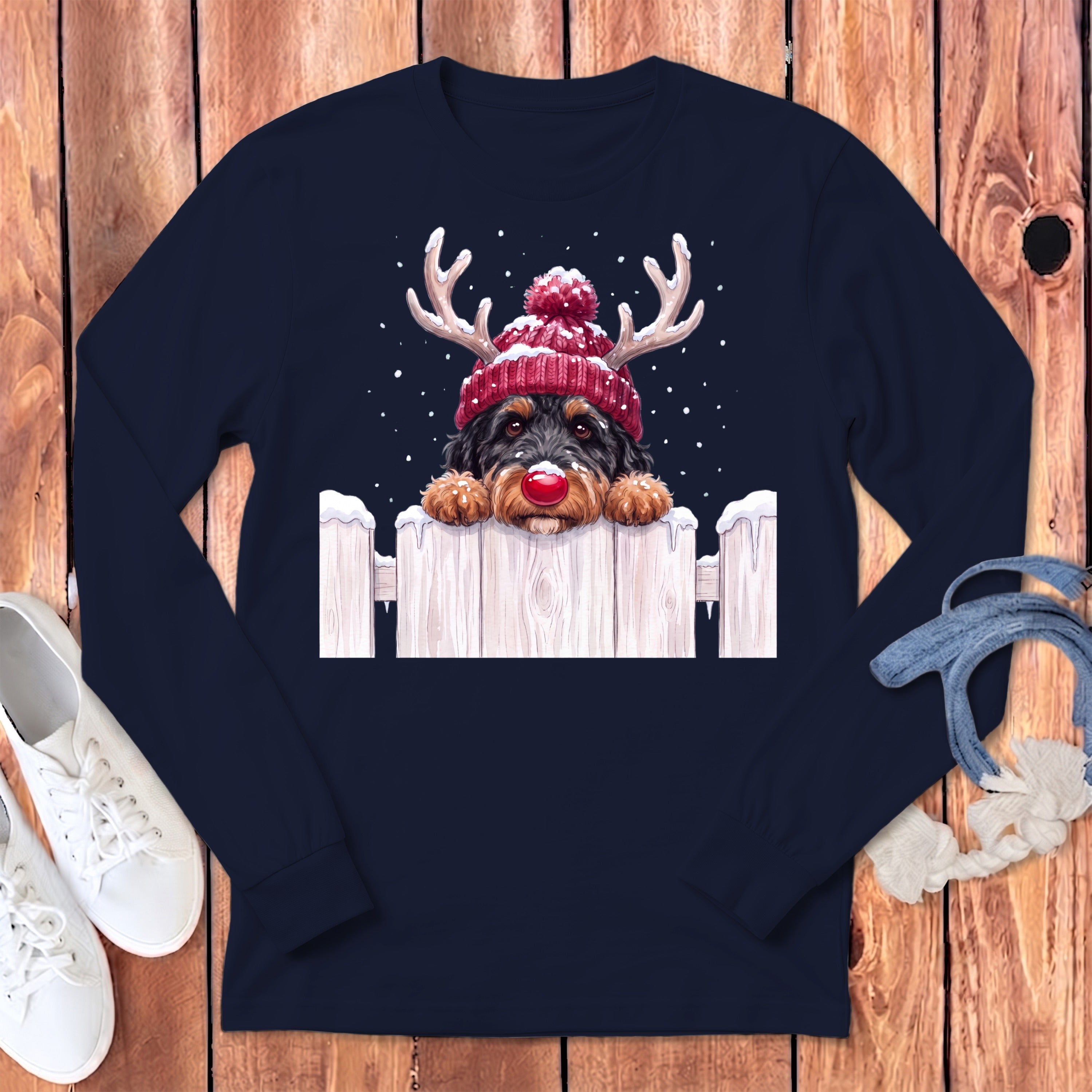 Dog in reindeer antlers and Santa hat peeking over a snowy fence.