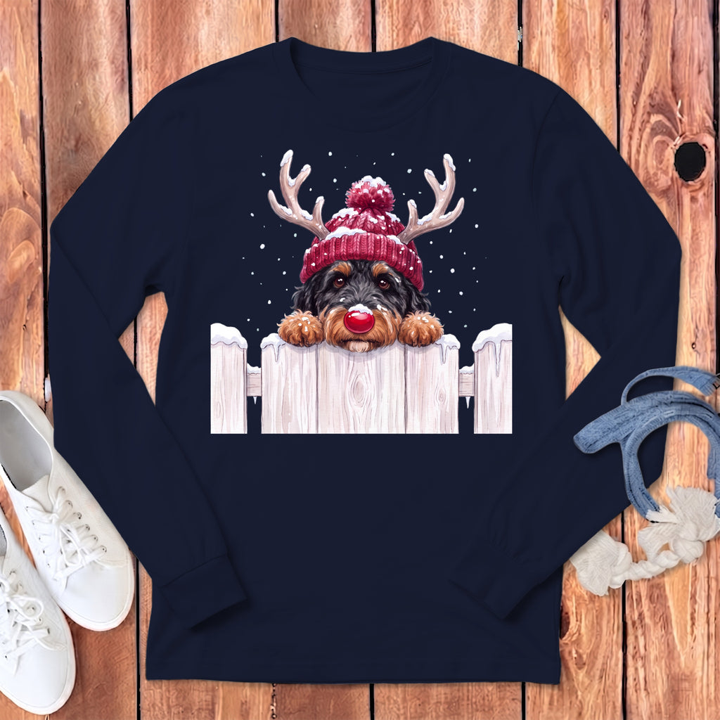 Dog in reindeer antlers and Santa hat peeking over a snowy fence.
