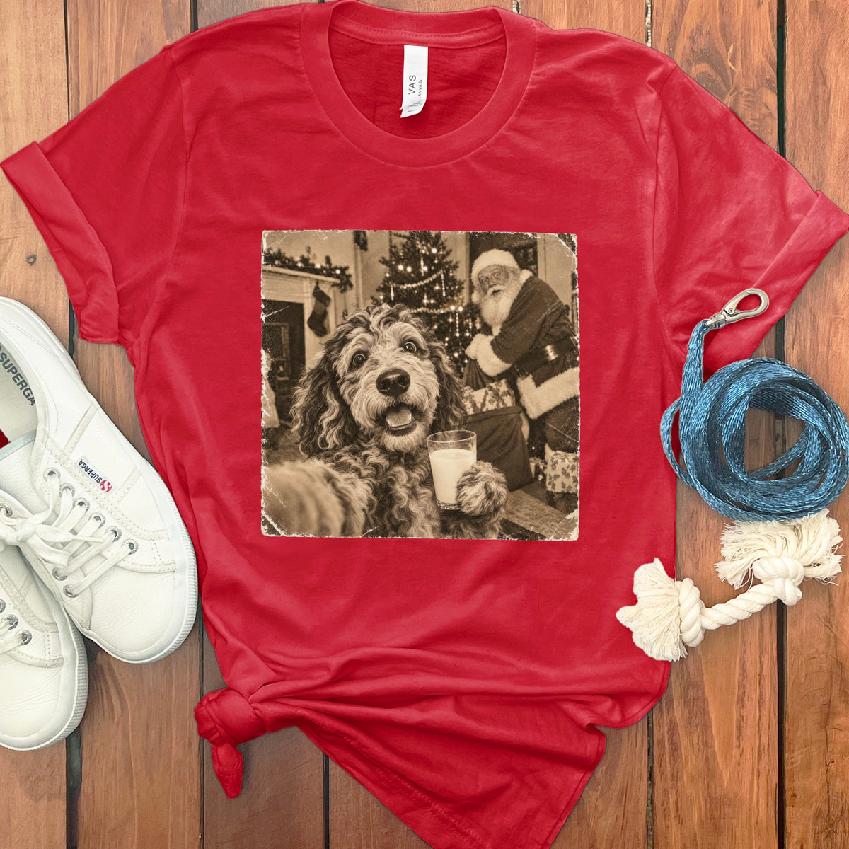 A red t-shirt printed with a vintage-style photo of a dog holding a glass of milk near Santa Claus.