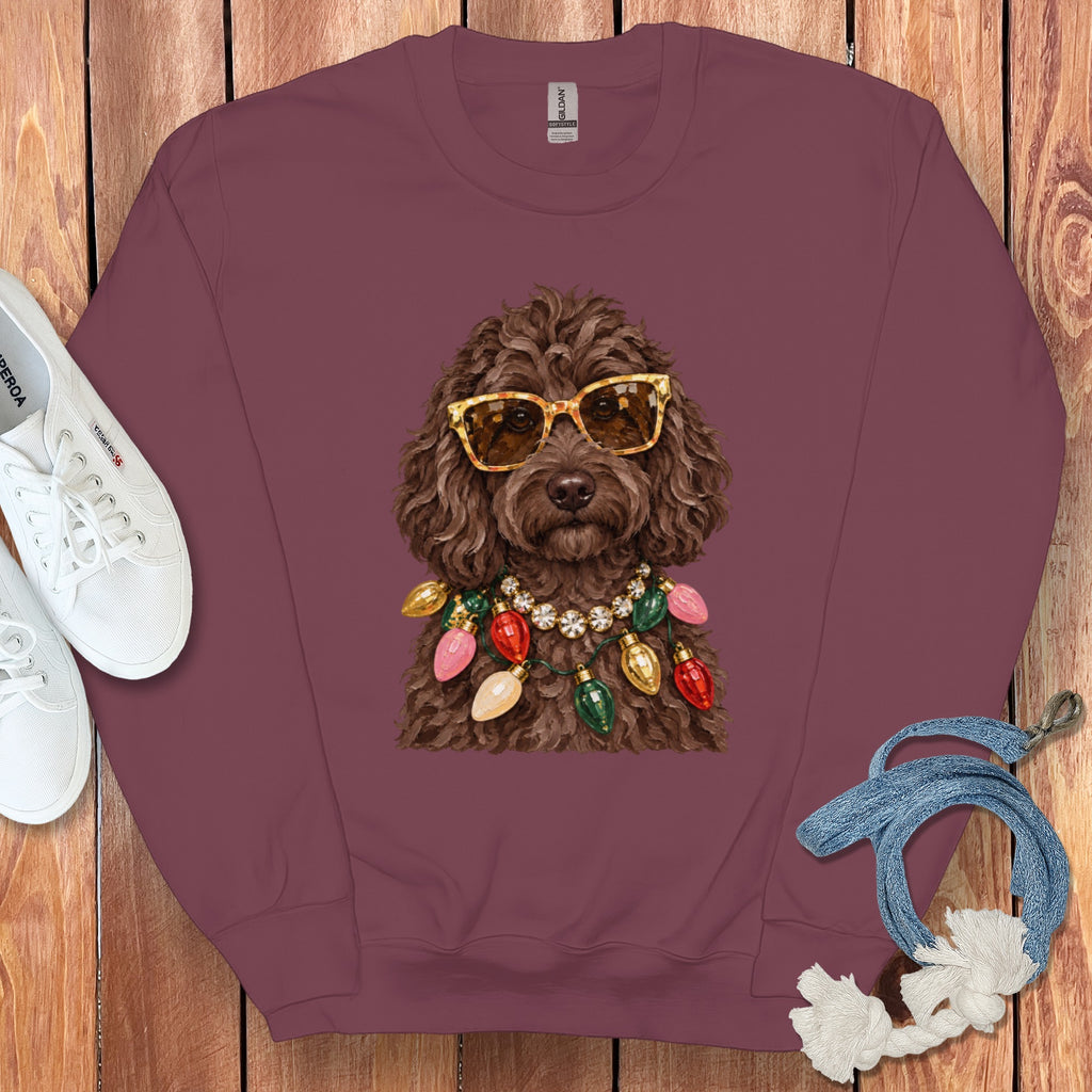 Brown doodle dog wearing sunglasses and Christmas lights necklace on maroon sweatshirt.