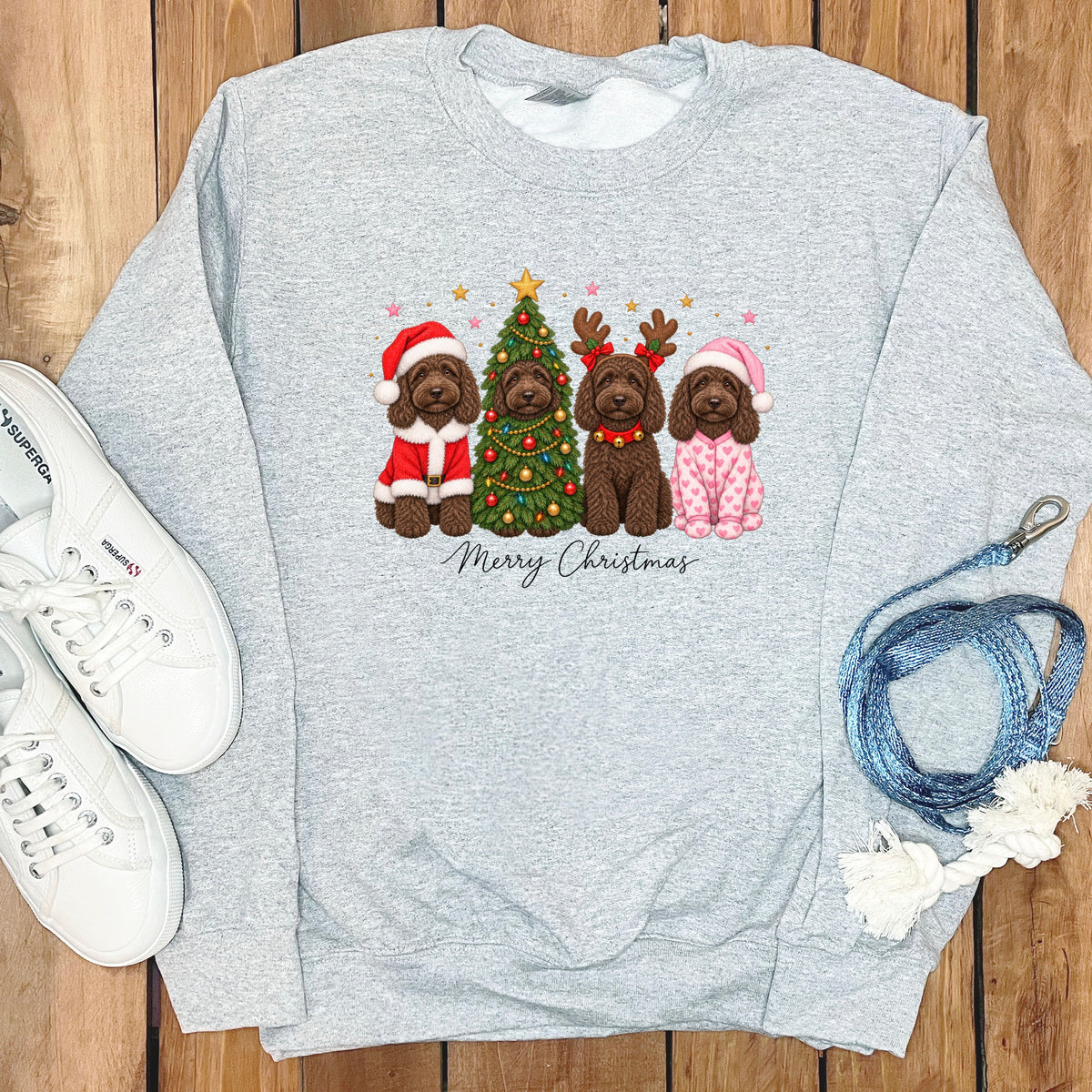 Grey crewneck sweatshirt featuring a graphic of four brown doodles celebrating Christmas, flanked by white sneakers and a blue leash.