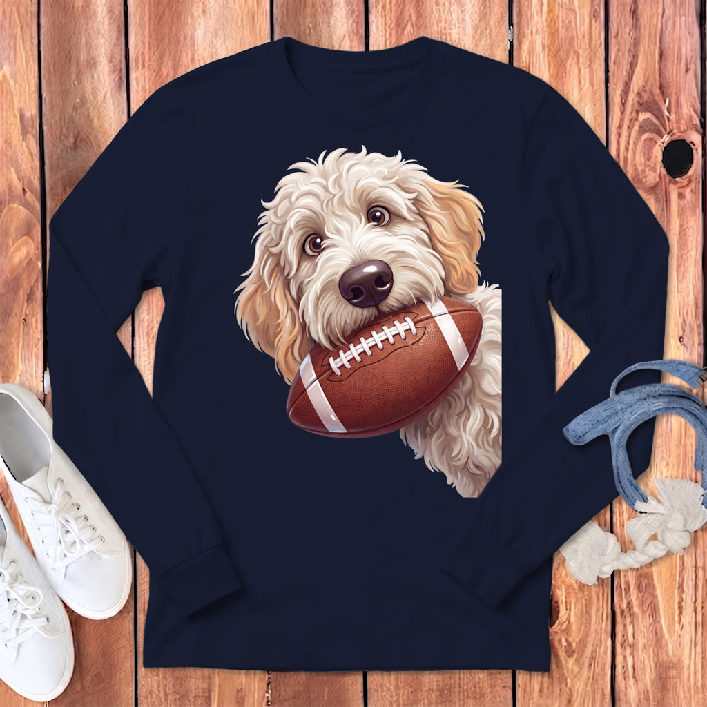 Fluffy white dog holding a football in its mouth on a navy long-sleeved shirt.