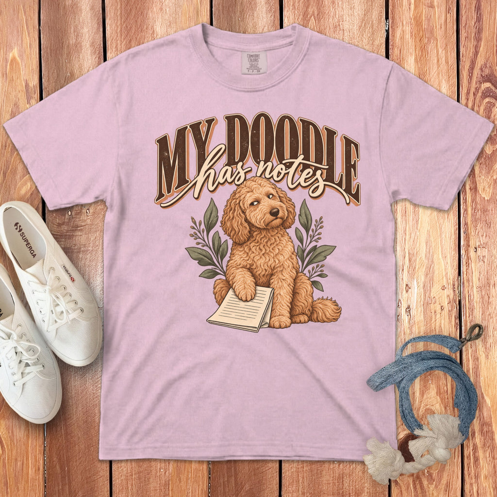 A pink t-shirt featuring a cartoon doodle dog holding a notepad with text above.