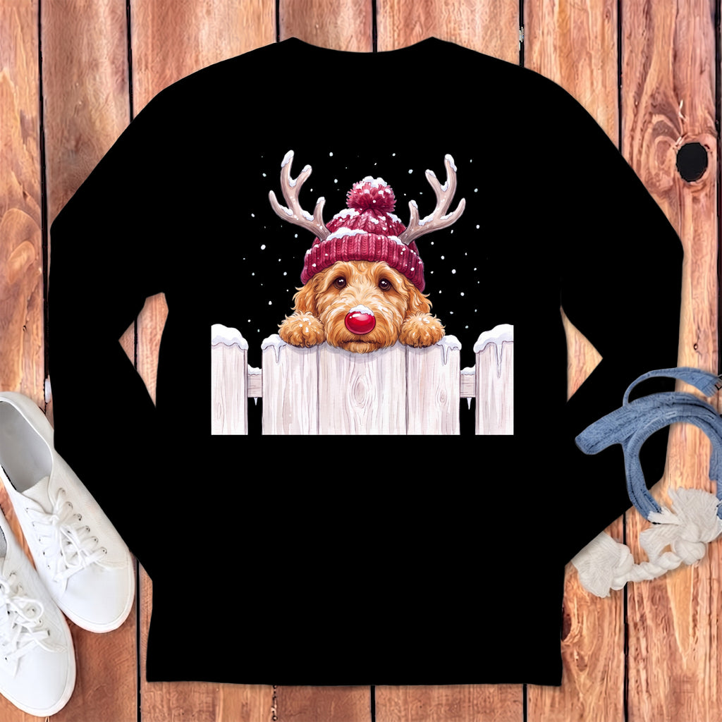 Golden doodle wearing a red beanie and antlers peeks over a wooden fence.