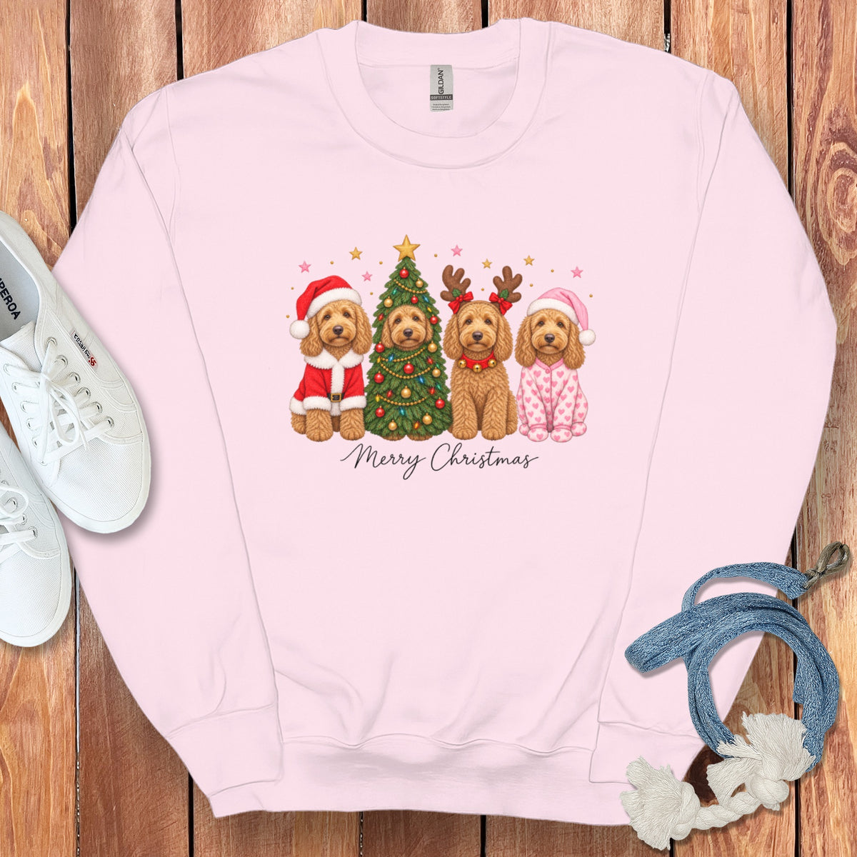A light pink crewneck sweatshirt featuring a graphic of four golden doodles dressed in holiday costumes with a Christmas tree.