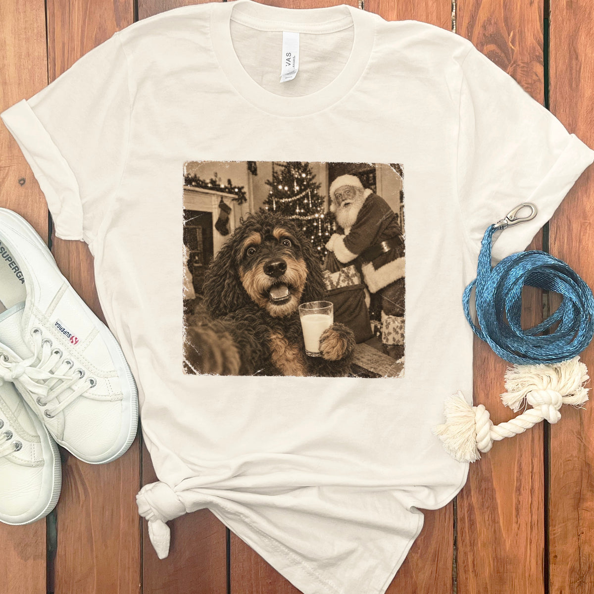 A cream-colored t-shirt with a vintage graphic featuring a fluffy doodle dog holding a glass of milk with Santa Claus in the background.