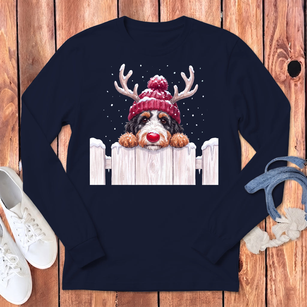 Bernese Mountain Dog in reindeer hat and red nose peeking over a snowy fence.