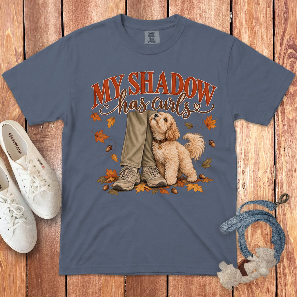 Blue t-shirt featuring a graphic of a fluffy dog beside a person's legs, surrounded by autumn leaves.