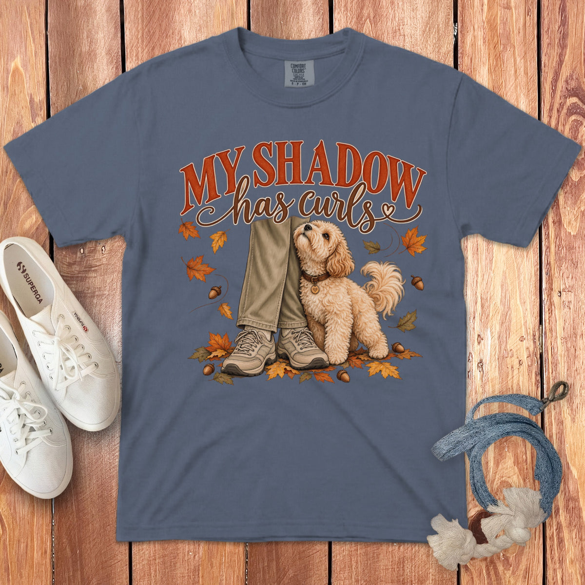 Blue t-shirt featuring a graphic of a fluffy dog beside a person's legs, surrounded by autumn leaves.