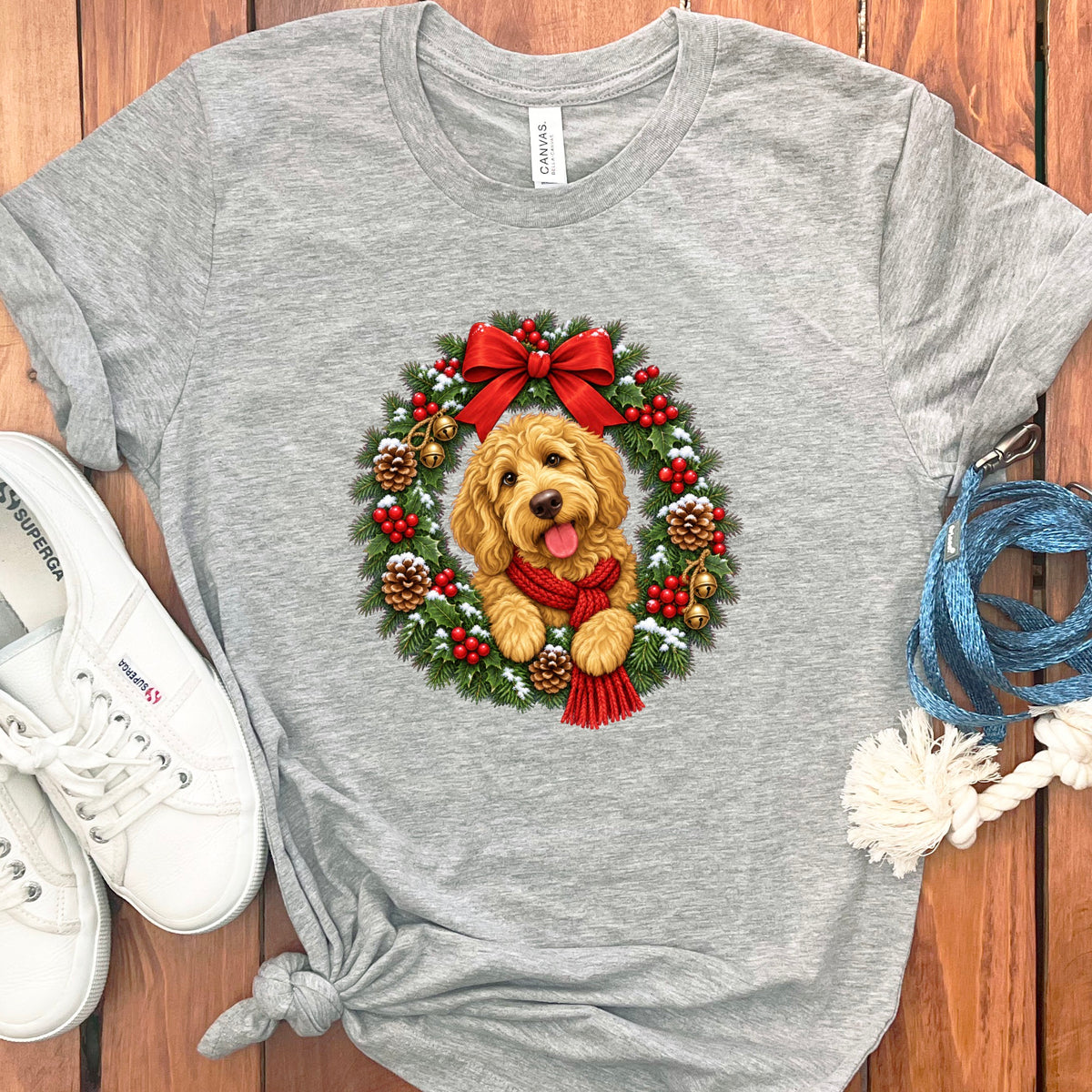 Heather gray t-shirt featuring a golden doodle dog inside a festive Christmas wreath, surrounded by accessories on a wooden background.