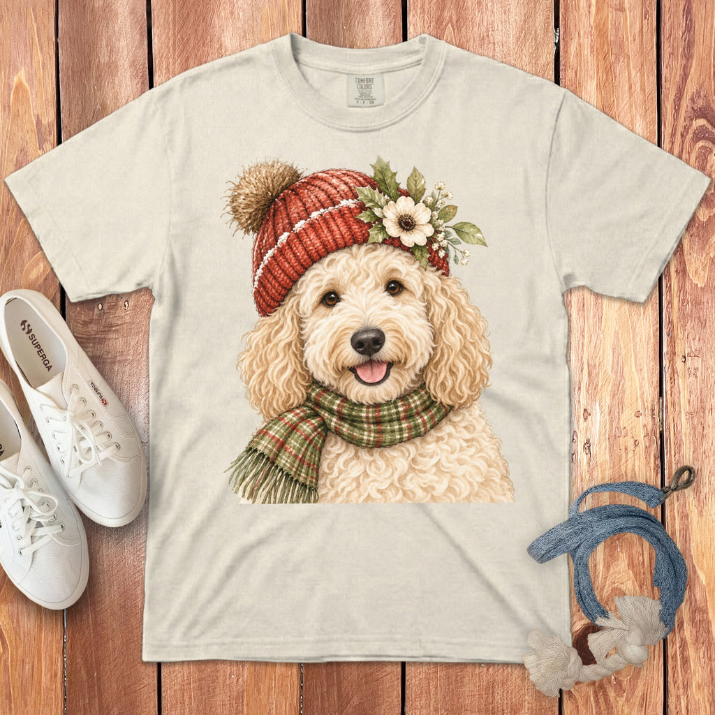 Cream t-shirt with a golden doodle wearing a red knit hat and plaid scarf.