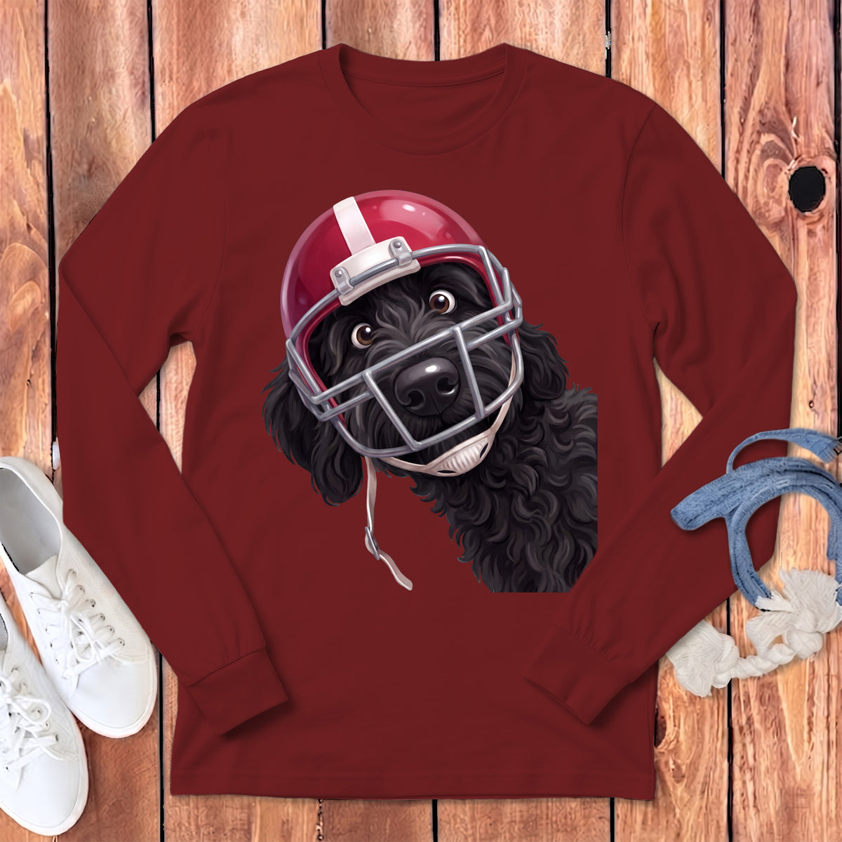 Black poodle wearing a red and white football helmet and facemask on a maroon shirt.